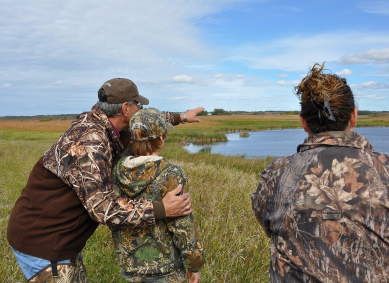 Two adults and a child in camouflage in front of a marsh