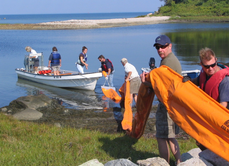 people holding oil boom next to water on Buzzards Bay