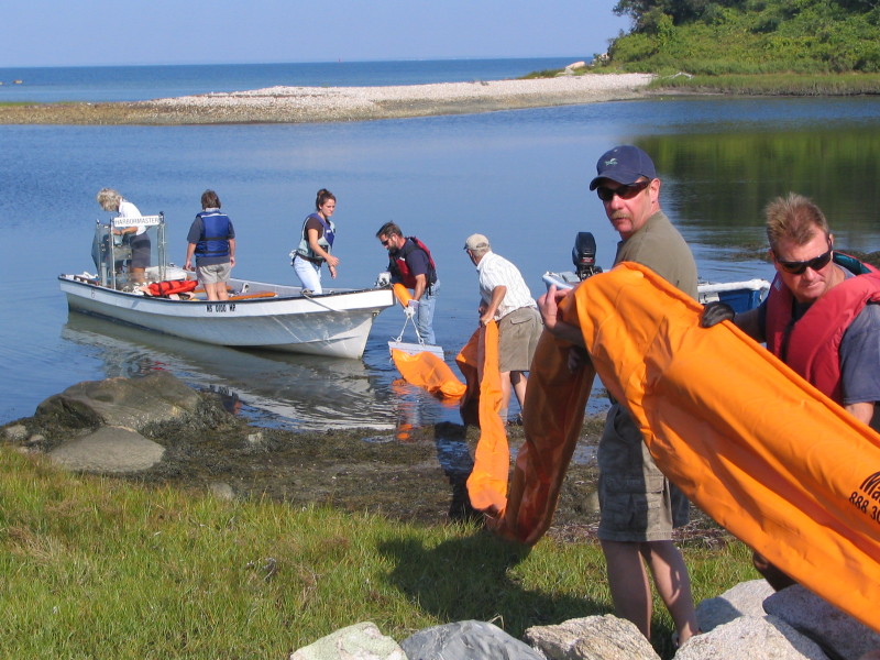 people holding oil boom next to water on Buzzards Bay