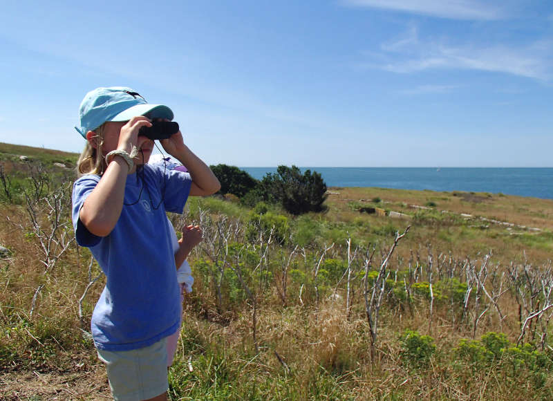 a girl looking at Buzzards Bay through binoculars