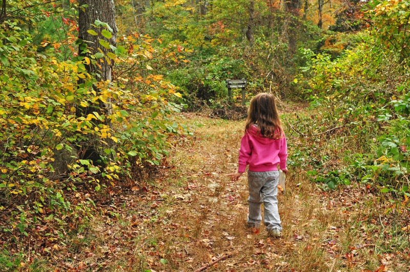 young girl walking down a trail through the woods