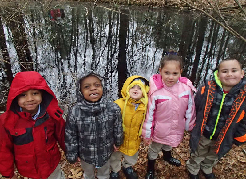four little kids standing next to a pond in the woods