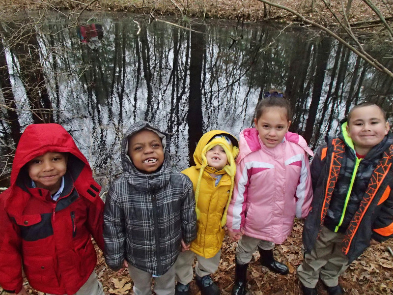 four little kids standing next to a pond in the woods