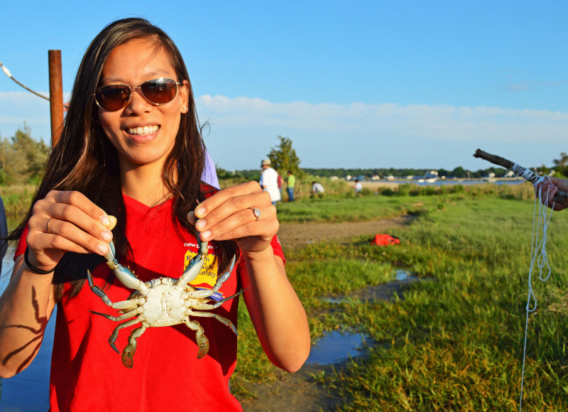 a woman holds up a blue crab in a salt marsh in Mattapoisett