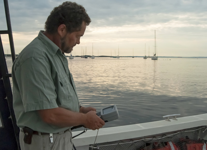 a man holds a water monitoring device on a boat in Mattapoisett Harbor