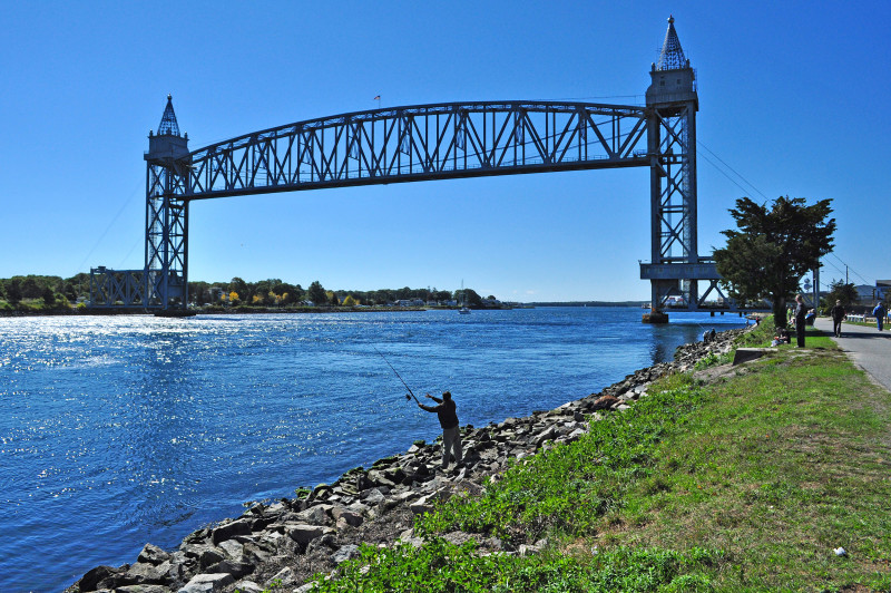 a man fishes from the shore of Cape Cod Canal next to the railroad bridge in Bourne