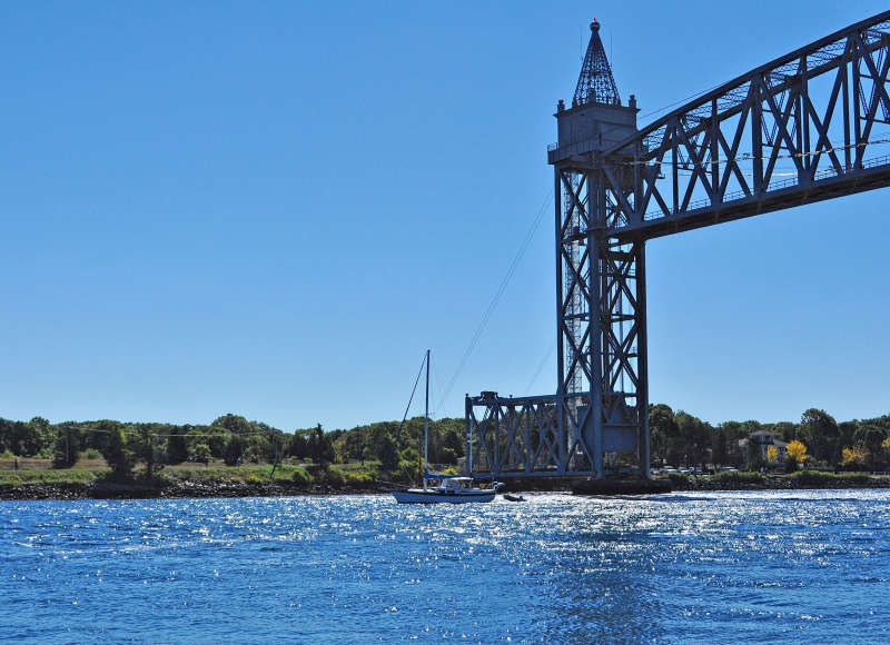 a sailboat crusing along Cape Cod Canal under the railroad bridge