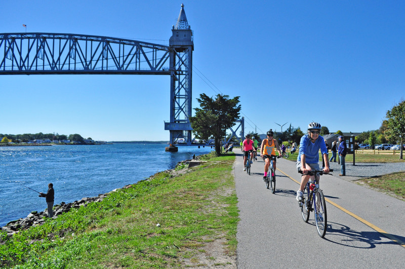 people bicycling and fishing along Cape Cod Canal next to the railroad bridge in Bourne