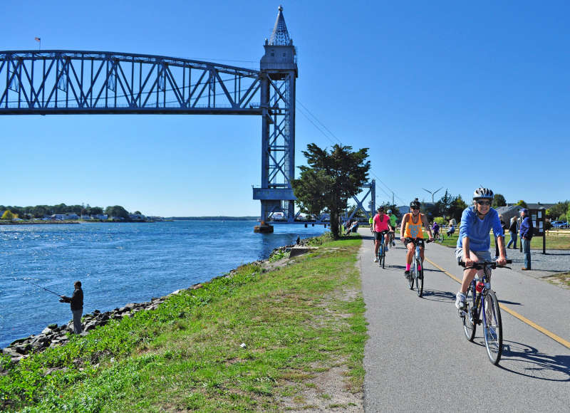 people bicycling and fishing along Cape Cod Canal next to the railroad bridge in Bourne