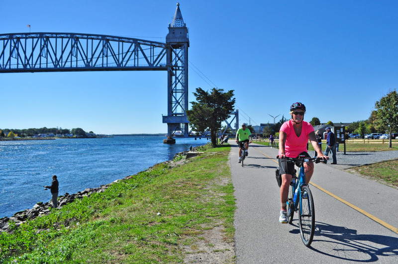 people bicycling and fishing along Cape Cod Canal next to the railroad bridge in Bourne