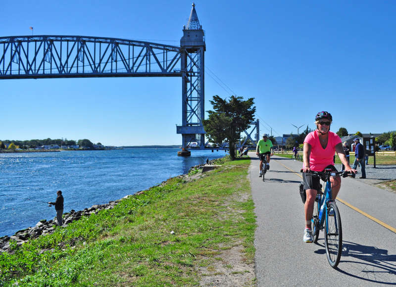 people bicycling and fishing along Cape Cod Canal next to the railroad bridge in Bourne