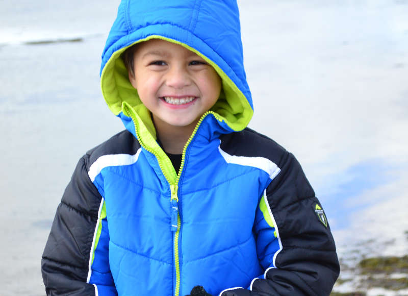 smiling boy holding a beach pail in winter at Little Harbor Beach in Wareham