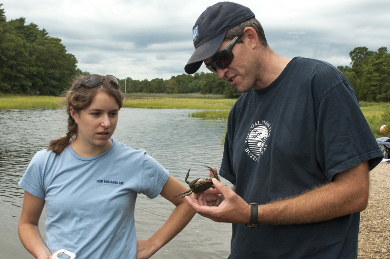 a man and a woman standing by the salt marsh at the Lyman Reserve in Bourne holding a blue crab