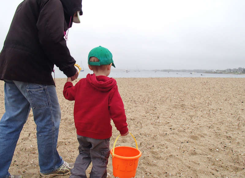 a mother and child walk on Monument Beach in Bourne on a cloudy day