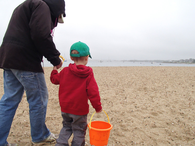 a mother and child walk on Monument Beach in Bourne on a cloudy day