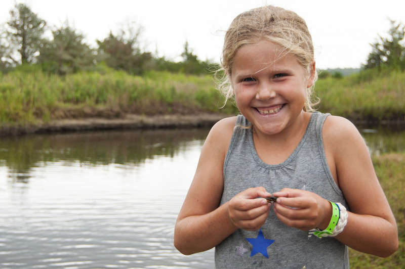 a young girl holds a small crab next to a salt marsh