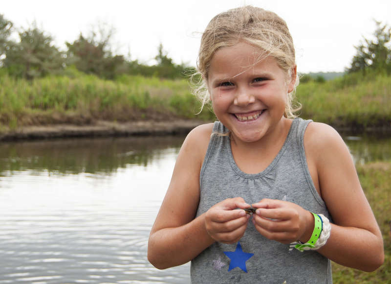 a young girl holds a small crab next to a salt marsh