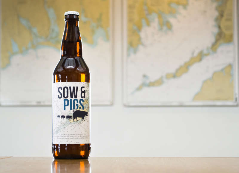 a bottle of Sow & Pigs Ale on a table with a map of Buzzards Bay behind it