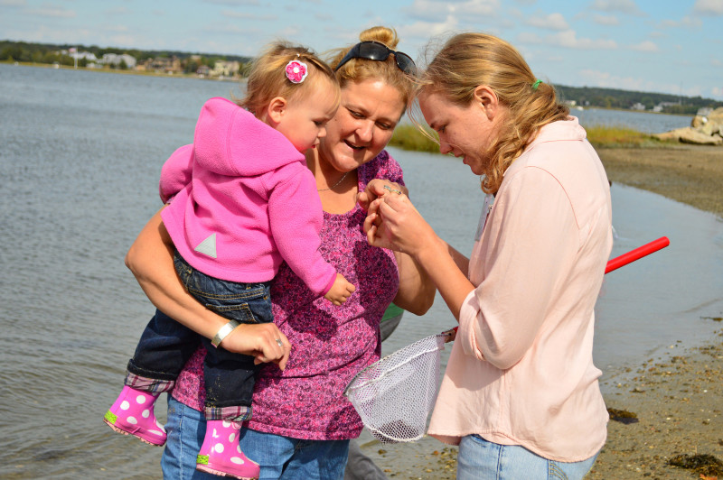 two women and a child looking at a shell by the water at Apponagansett Park in Dartmouth