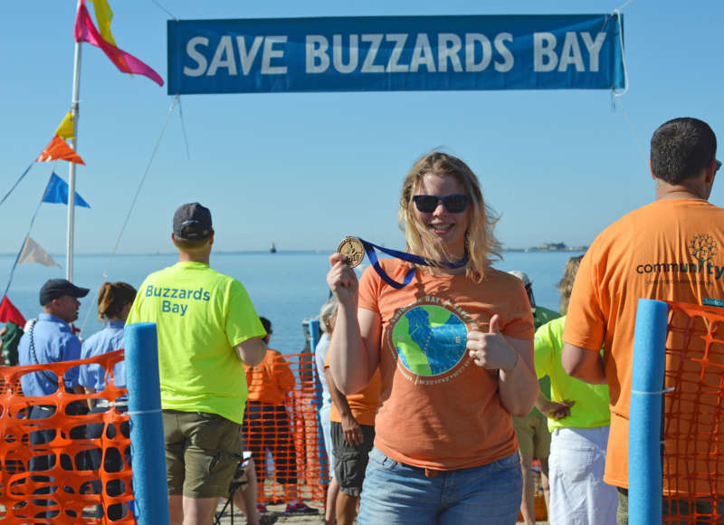 a woman holding up her medal at the Buzzards Bay Swim