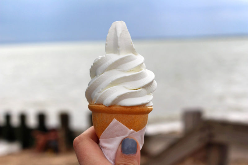 hand holding an ice cream cone in front of the ocean