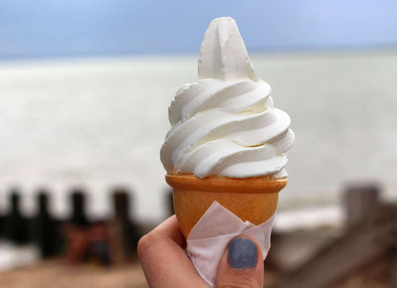 hand holding an ice cream cone in front of the ocean