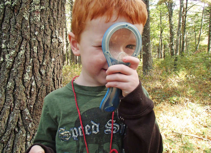 a boy holds a magnifying glass to his eye while exploring the forest