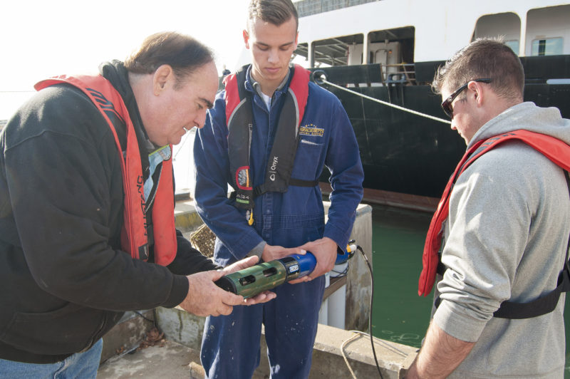 Massachusetts Maritime Academy professor and students standing by the water holding a sonde