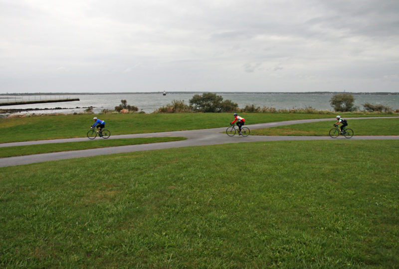 three cyclists riding on a bike path past the water at Fort Taber Park in New Bedford