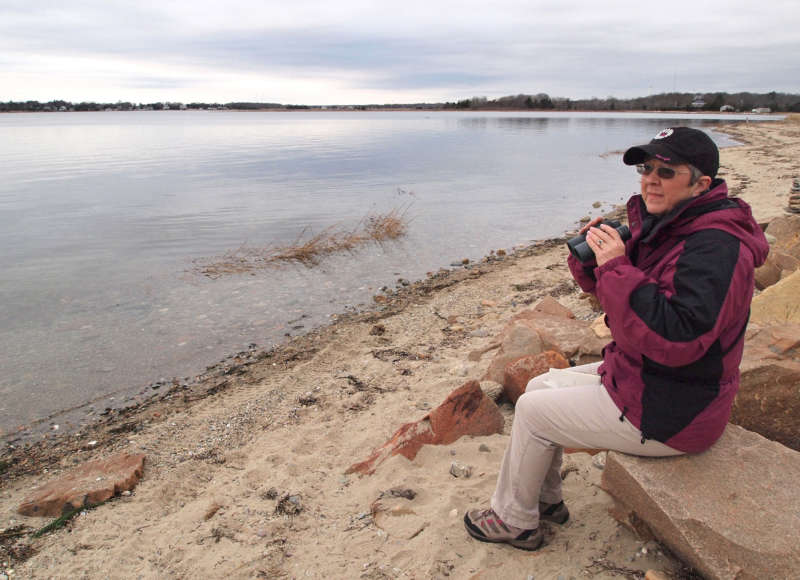 a woman sitting by Nasketucket Bay in Mattapoisett holding a pair of binoculars