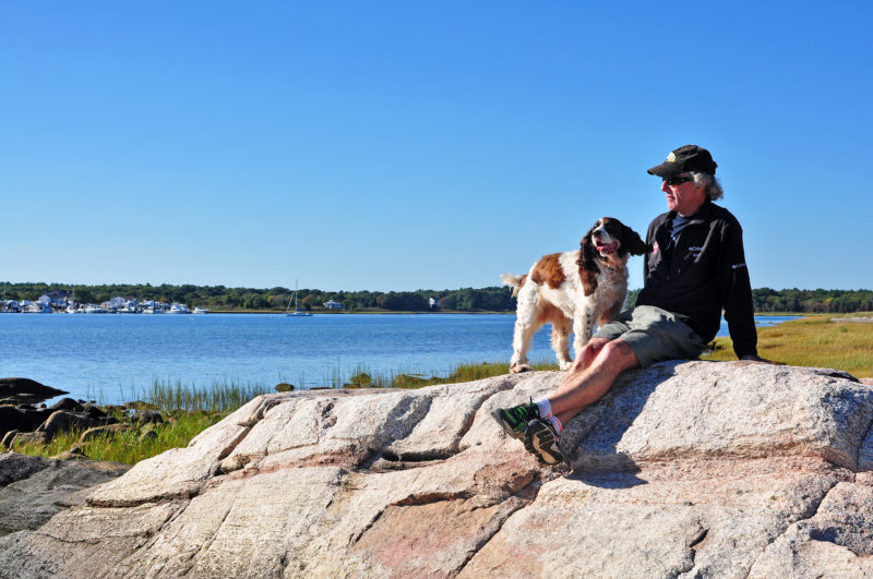 a man and a dog on a large rock at the Munn Preserve in Mattapoisett