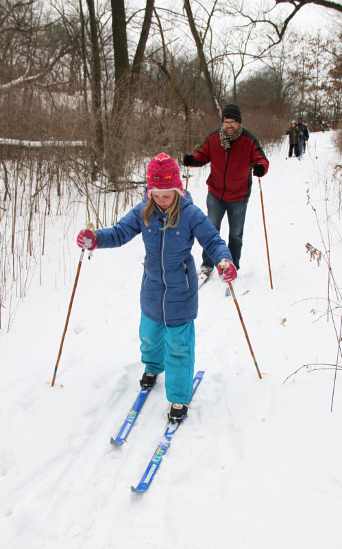 a family cross-country skiing on a trail in the woods