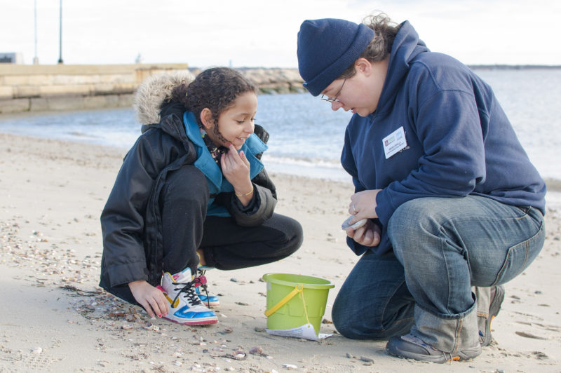 student and educator on a beach looking at a shell