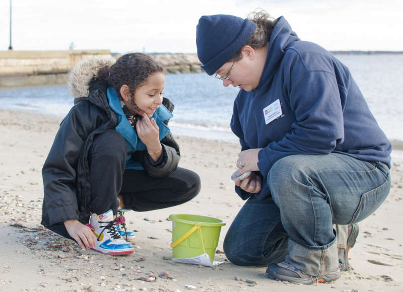 student and educator on a beach looking at a shell