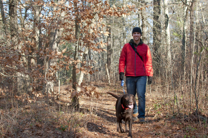 a man walking a dog on the trail through the woods at Halfway Pond Conservation Area in Plymouth