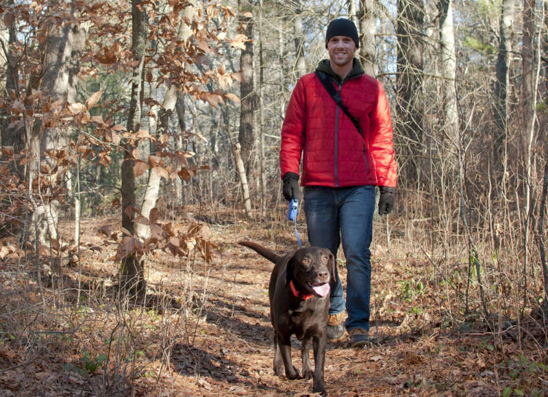 a man walking a dog on the trail through the woods at Halfway Pond Conservation Area in Plymouth