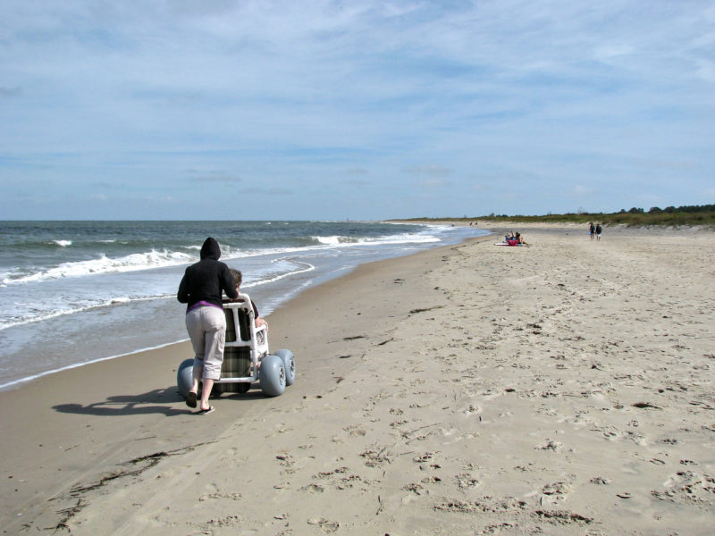 woman pushing a person down a beach in a wheelchair