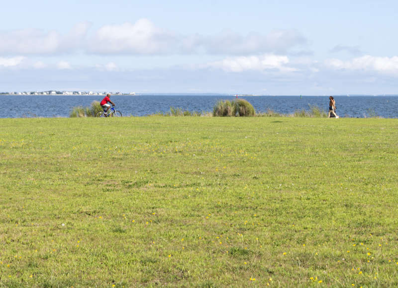 people walking and riding bikes along the water at Fort Taber Park