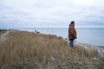 A man standing by the shoreline looking out over Buzzards Bay at Gooseberry Island.