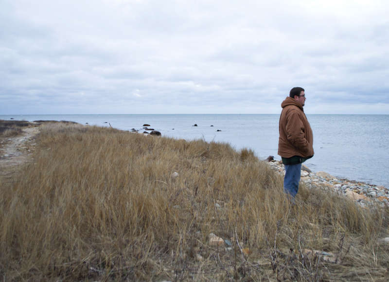 A man standing by the shoreline looking out over Buzzards Bay at Gooseberry Island.