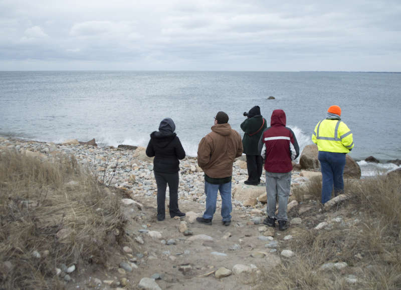 A group of people standing by the shoreline looking out over Buzzards Bay at Gooseberry Island.