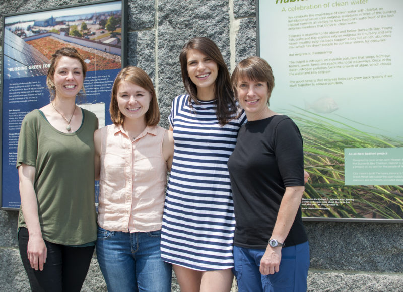 Four new staff members standing outside the Coalition’s stone building, with signs about green energy and clean water in the background.