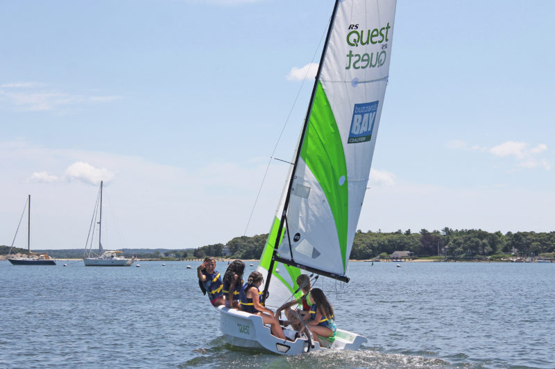 Four kids and a CBC instructor heading out on a white sailboat with green and white sails.