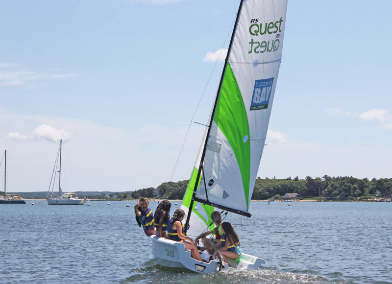 Four kids and a CBC instructor heading out on a white sailboat with green and white sails.