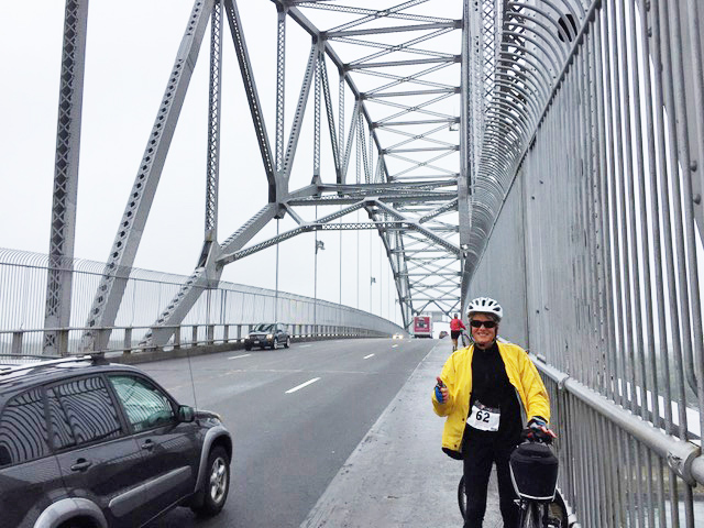 Biker Tanya Roy, in a yellow jacket, glasses and helmet, crossing the span of the Bourne Bridge.