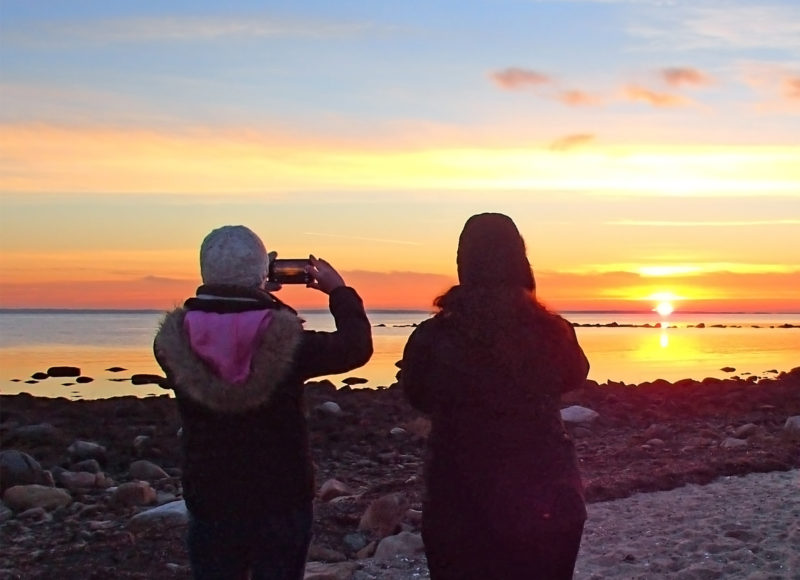 A woman taking a photo of a sunset with her phone