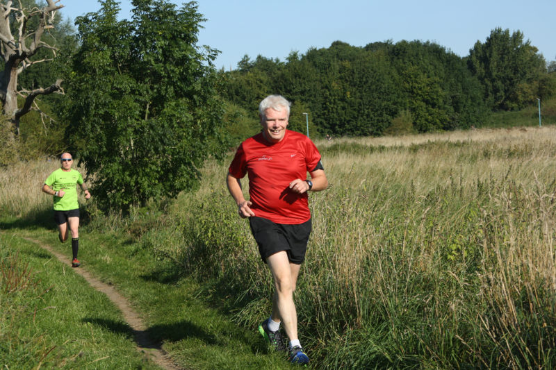 Two men running on a trail next to a field