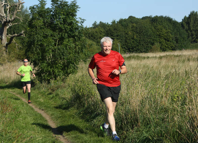 Two men running on a trail next to a field