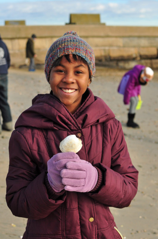 A smiling girl holding up a quahog shell on East Beach