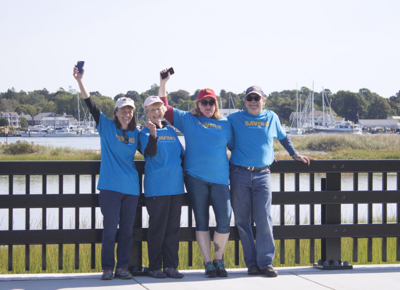 Volunteers in blue shirts on a bridge cheering on cyclists in the Buzzards Bay Watershed Ride